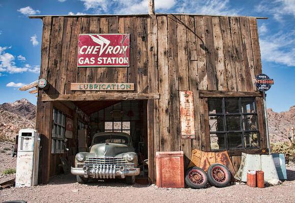 An old fashioned wooden gas station with an old Cadillac parked in one garage bay.  The Chevron gas station sign is on top of the garage.  This image was taken at a kept up ghost town named Nelson in Nevada.  Nelson is about 20 minutes from the Hoover Dam.