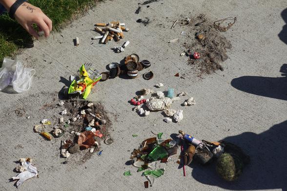 Photo shows wastes collected earlier sorted on concrete sidewalk into piles of glass, cigarette butts, bottle caps, plastics (Styrofoam, predominantly) and other like materials to help kids understand where the wastes originated.