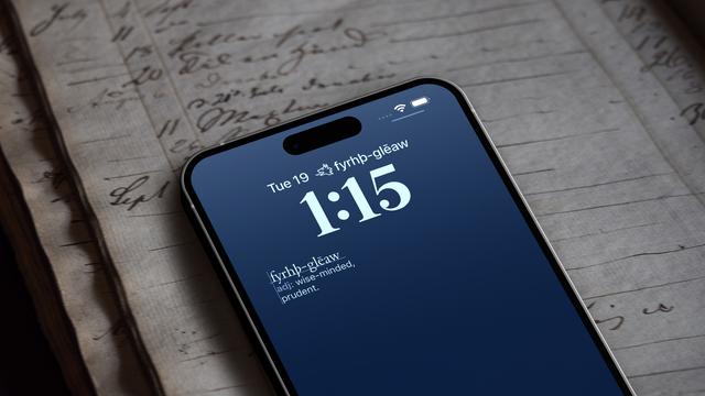An iPhone with the Old English word of the day lock screen widgets. The inline widget above the date shows a dragon symbol and the word fyrhþ-glēaw. The larger rectangular widget below the time  has the same word and the definition wise-minded, prudent. The iPhone sits on an old hand-ruled ledger full of handwritten notes.
