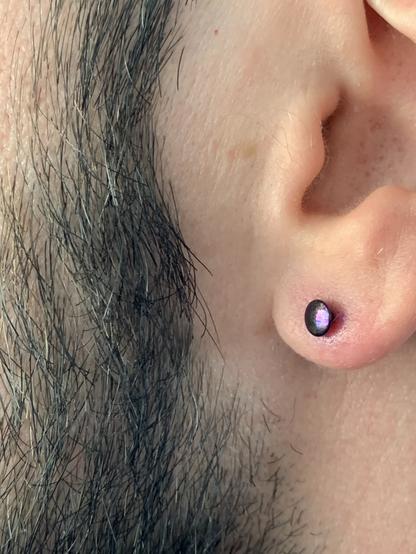 Close-up of the man’s ear, showing the metallic purple earring. It’s a stud, with the disc side at the front.