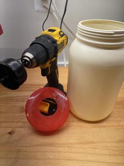 Cutting a hole in the lid of a protein powder bin using a 2-inch hole drill bit.