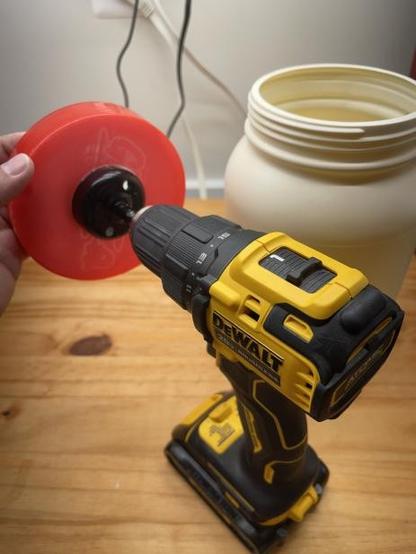 Cutting a hole in the lid of a protein powder bin using a 2-inch hole drill bit.