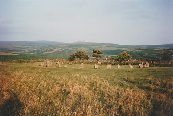 A colour photo taken in 1994 of the prehistoric stone circle at Brisworthy on Dartmoor. The circle is about 25m across and has 24 stones remaining out of the original 42. The Trowlesworthy Tors and the hills on the southern edge of Dartmoor can be seen in the distance.
