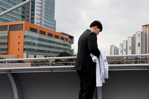 Ryu O. Hada, 25, holds his white coat in front of the hospital where he worked in Seoul. REUTERS/Kim Soo-Hyeon