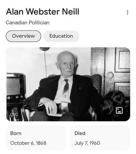 A picture of Neill sitting in a chair. He is an old man in a suit and tie.