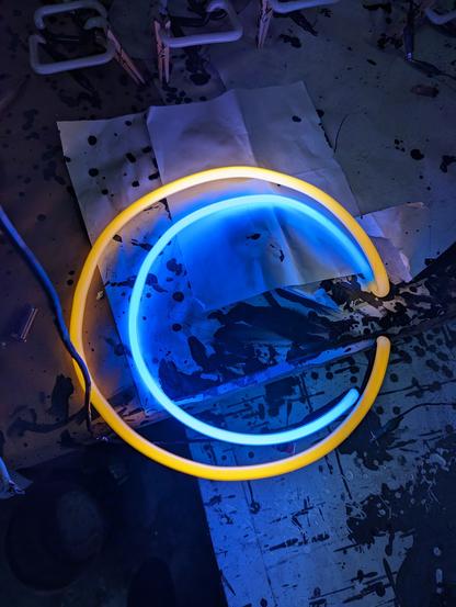 A dramatic crescent moon design with the outside a yellow tube and the inside a dark blue tube hanging off of a messy paint dripped table.