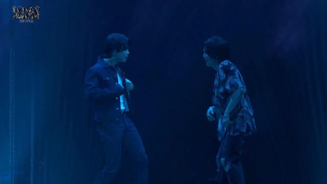 Jimin and Yoongi onstage for the D-Day concert, performing Tony Montana. The light is very blue. They're looking at each other.