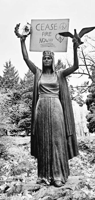 Ceasefire Now, cardboard protest sign. Placed in crown female peace statue. It's a monument to the Mackenzie Papineau Battalion.
Black and white photo.