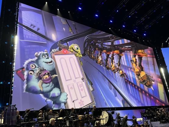 An inverted (hanging) roller coaster going through the door vault from Monsters Inc, passing by a door with Mike, Sulley, and Boo riding on it.