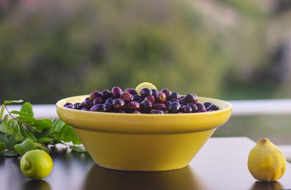 A yellow ceramic bowl is filled with olives that are somewhere between green and black in colour and ripeness - one might call them purple I guess.

They have been cut and rinsed for several weeks to remove the bitter compounds and are ready to be jarred in brine.

The bowl is surrounded by some of the ingredients we add to the brine, namely a couple of lemons and leaves of a carob tree.