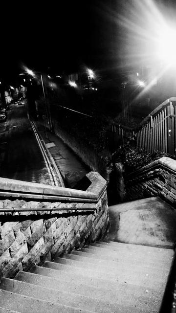 Looking down the second flight of steps at night, stone wall on the left railings to protect trespass onto the adjacent railway line on the right