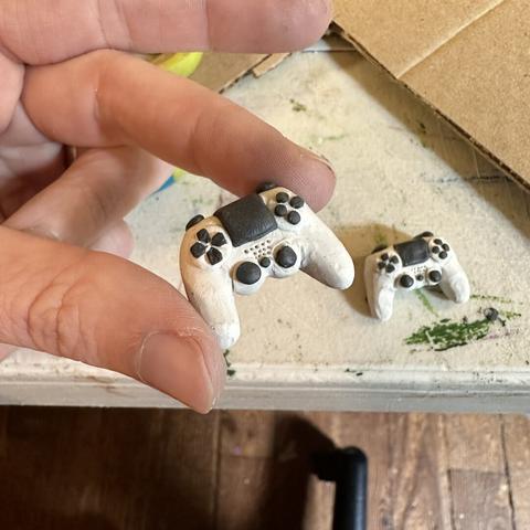 A hand holds a miniature clay playstation controller