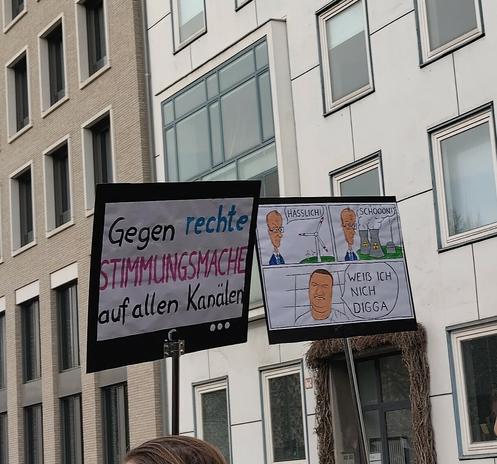 2 Plakate:

"Gegen rechte Stimmungsmache in den Medien" 

auf dem 2. sind 3 Cartoons:
1 - Friedr Merz vor Windrad: "Hässlich"
2 - Friedr Merz vor AKW: " Schööon"
3 - junger Mann: "Weiß ich nich Digga"
