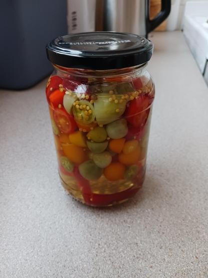 a jar filled with small chillis and tomatoes of various colours