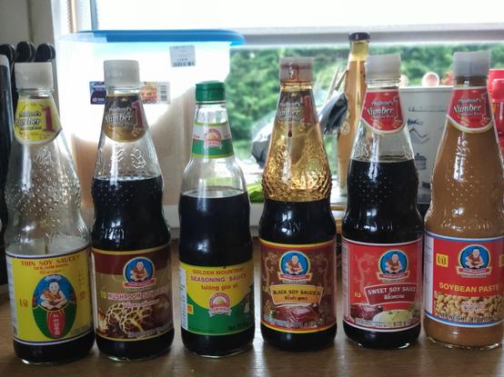 A row of six thai soy sauce bottles sitting on a wooden kitchen surface