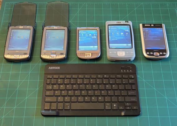 4 of my iPaqs and my Dell Axim X51V lined up with the screens turned on.  Below them sits the Arteck keyboard.  It is hard plastic and black in color. It has white lettering on it’s chiclet style keys.