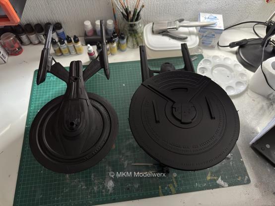 Two models sitting on a green cutting mat on a white table. Both models are painted black.