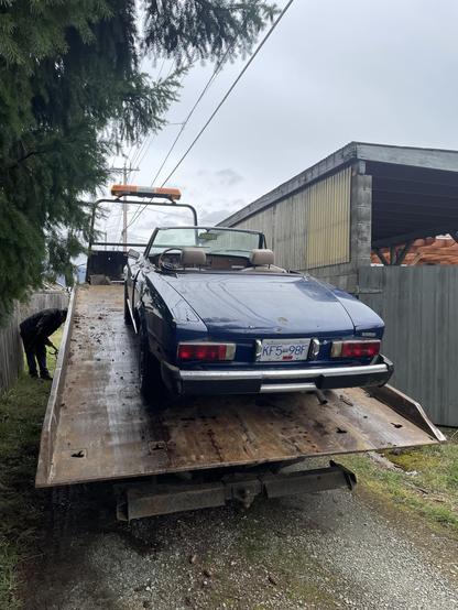 A small blue convertible is raised a top of flatbed tow truck