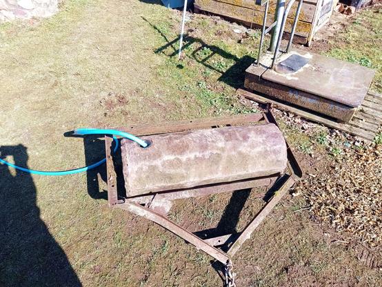 An agricultural roller for towing behind a tractor. Actually this is one part of a three-roller but that would be too large and the other wasn't in good shape. A blue hose is stuck into the filler hole, slowly filling the inside of the roller with water ballast to increase its weight to about 250 kg give or take.