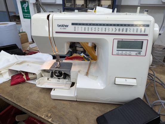 Another repair candidate, this time a sewing machine is being worked on. The lower bobbin compartment is open. The foot pedal is on the bench to the right in the foreground.