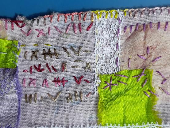 A detail shows wild stitching in variegated thread (red, pink, and green nuances) that looks like writing in an unknown language. Some other scraps are fixed with unregular purple embroidery: green saree silk, used teabag paper and lace.
