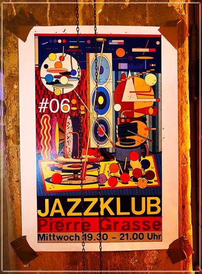 A poster in a club.
On the poster there are many abstract shapes, circles, triangles, rectangles e.t.c., in many different colours and sizes.
The poster reads (on the bottom): „JAZZKLUB
Pierre Grasse
Mittwoch 19.30 - 21.00 Uhr“
