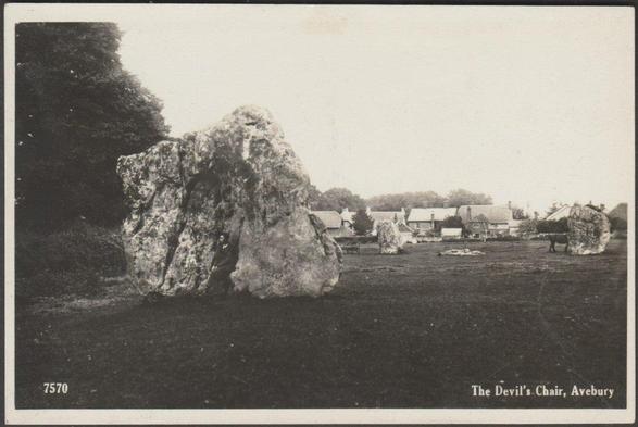 A vintage postcard showing the massive standing stone known as the Devil's Chair within the huge Avebury complex of stone circles and avenues in Wiltshire. A gentleman sits in the hollow of the stone, gazing off to the side in mellow contemplation. Other massive stones can be seen behind and a horse is on the right, partially obscured by one of the megaliths. Some of the cottages in the village of Avebury, which lies partly within the huge megalithic arrangement, can be seen in the background.