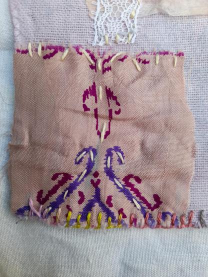 A very small saree silk scrap. It's bright rosé with an ornamental print in purple and dark red. The wild stitches follow the ornament.