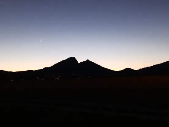 Au crépuscule, une montagne totalement noire se découpe dans un ciel dégagé aux lumières du soleil couchant. On distingue à peine un croissant de lune.