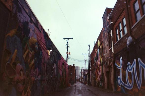 A narrow alleyway lined with buildings covered in colorful street art and graffiti.