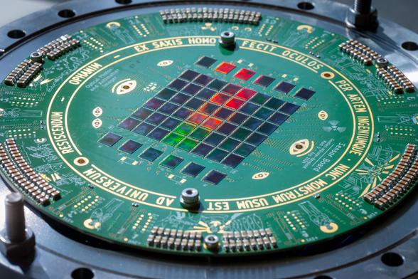 A circular PcB measuring about 20 cm in diameter with a grid of camera sensor dies soldered in its middle. At the outside of the PCB, there is a ring of large ceramic capacitors. There are no other components visible. The PCB has green solder mask and uses gold plating. It shows a fucking metal design around the sensor grid with several stylized eyes shown in gold plated solder mask openings. A ring around the sensors contains a Latin inscription reading “Ophanim - ex saxis homo fecit oculos per artem ingeniumque. Numc Monstrum usum est ad Universum resiscendum”. The outside of this ring contains illustrations of a hunch of angels with halos and shit wrapping around the board.