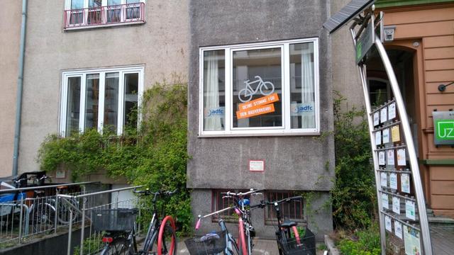 Fensterfront des ADFC-Infoladen mit neuer Beschriftung. Ein aufwärts fahrendes Fahrrad in weiß mit Schriftzug drunter "Deine Stimme für den Radverkehr" in weiß auf orangem Grund. Links und rechts in kleinen Fensterflügeln das Logo des ADFC mit dem Schriftzug "ADFC Region Hannover"