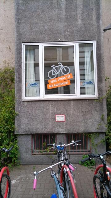Fensterfront des ADFC-Infoladen mit neuer Beschriftung. Ein aufwärts fahrendes Fahrrad in weiß mit Schriftzug drunter "Deine Stimme für den Radverkehr" in weiß auf orangem Grund. Links und rechts in kleinen Fensterflügeln das Logo des ADFC mit dem Schriftzug "ADFC Region Hannover"