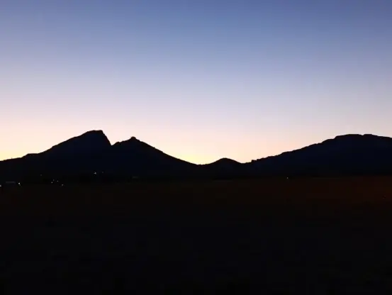Au crépuscule, une montagne totalement noire se découpe dans un ciel dégagé aux lumières du soleil couchant. On distingue quelques éclairages ici et là dans les parties obscures de la photo.