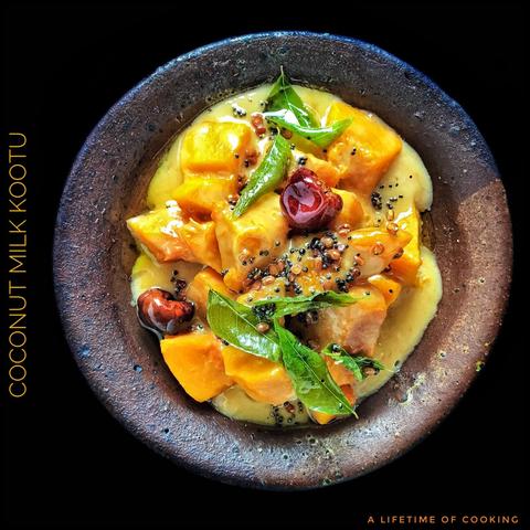 A bowl of yellow curry of pumpkin and coconut milk, topped with bright green curry leaves and red sambar chillies.