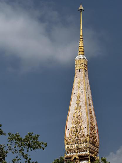 Closer shot of the Wat Chalong tower, in golden sunlight under a blue sky with wispy white clouds.