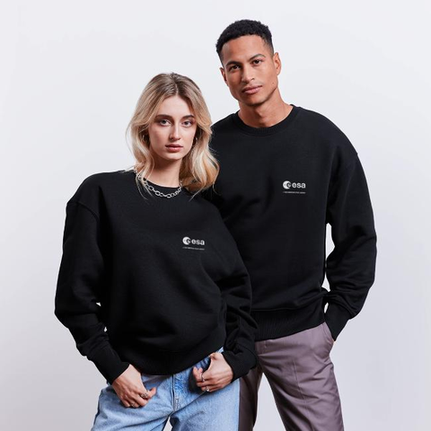 The photo shows a blonde woman and a dark-haired man. They are wearing a black sweatshirt with the ESA logo on the left side. The logo is written in white.