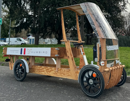 Ein überwiegend aus Holz gebauter Fahrrad-Pickup, der vorne eine offene, überdachte und mit einer Frontscheibe versehene Kabine hat, und dahinter eine recht lange Ladefläche, die viel Stauraum bietet. Ökologisch und stylisch!