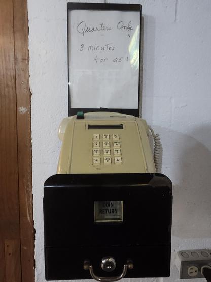 a push button telephone from probably 1972 with a hand written sign above that says "Quarters Only: 3 minutes for 25 cents" and a black lockbox below that accepts quarters.