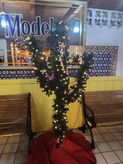 An artificial saguaro made of artificial christmas tree branches, and covered in festive lights and easter decorations.