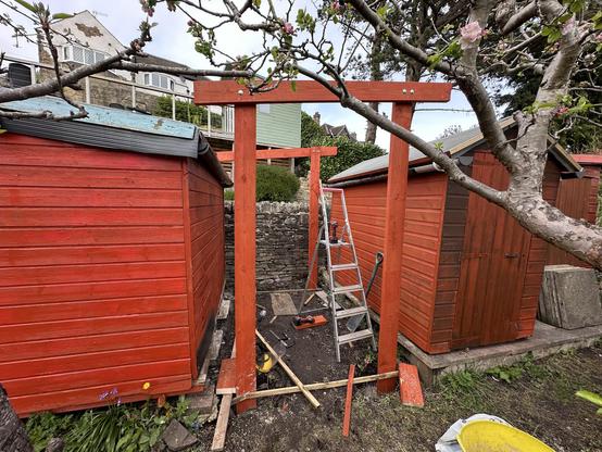 Two red sheds with a gap between. In the gap are four vertical post with two crossbeams at the top. All the wood is stained red. It looks a bit like a temple.