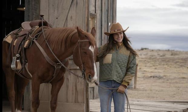 Minka Kelly in jeans an a Stetson leads a brown horse from a barn in Ransom Canyon.