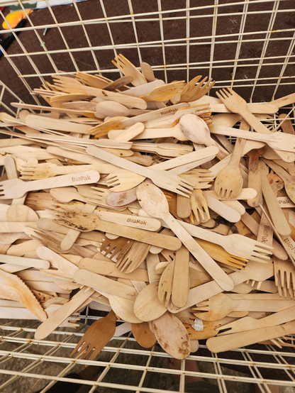 A wire basket filled with hundreds of used bamboo disposable forks and spoons.