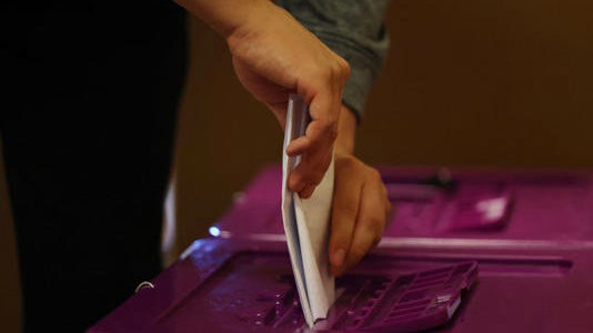 A voter slips their folded ballot paper into the slot of a purple vote-collector on the first day of early voting in Sydney.