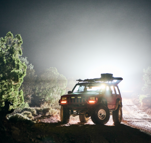 A jeep at night, with light shining from behind it. The front tires are both pointed inwards because the tie rod fell off.