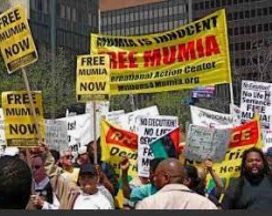 Demonstrators with yellow signs that read: Free Mumia Now!
