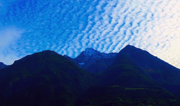 Pockmarks of white cirrus clouds against a blue sky over some mountains, the middle of which is particularly tall and covered in snow