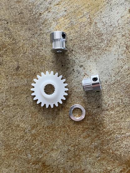 3D printed white plastic gear, next to two timing pulleys. One pulley has the top belt guide popped off