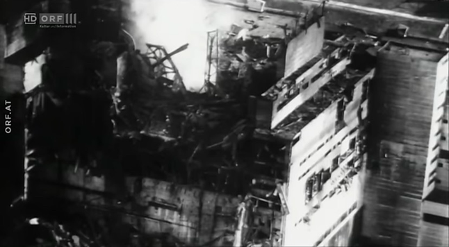 Erstes Foto des explodierten Reaktors: Zerstörung der Dachkonstruktion, zerborstener Stahlbeton und verbogene Stahlträger. In der Mitte ein Glühen und Qualm, verursacht durch die schmelzenden Brennstäbe und brennenden Graphit.