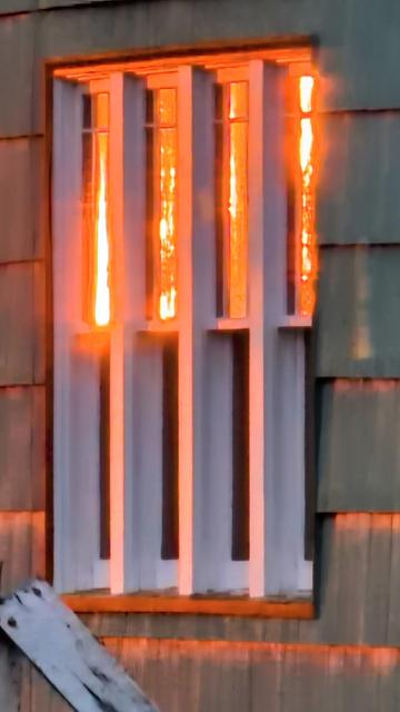 Reflection of the brilliant orange sunrise in a partitioned white window.